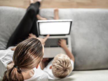 Mother sitting with child learning at home on the computer.